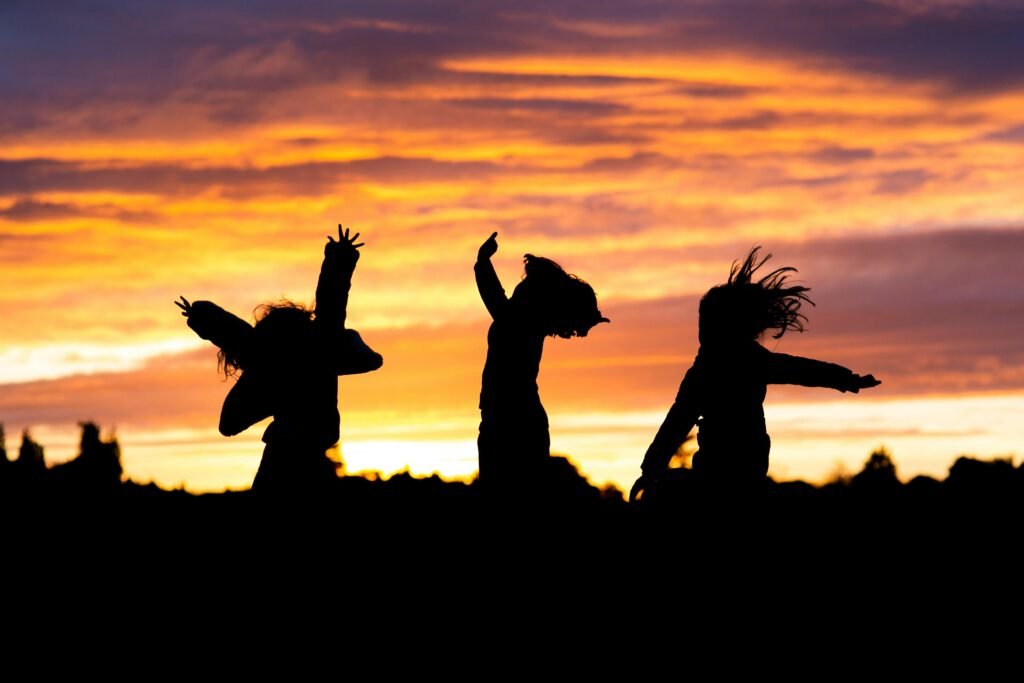 Energetic kids dancing in silhouette during a vibrant sunset, showcasing youthful joy and freedom.