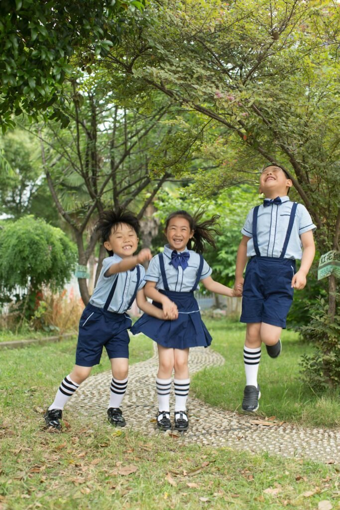 Three joyful children in school uniforms playing together outdoors on a bright day.