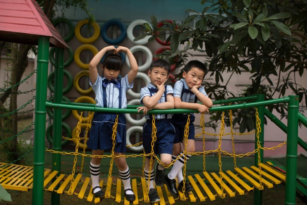 Three children in uniform having fun on a vibrant playground bridge outdoors.